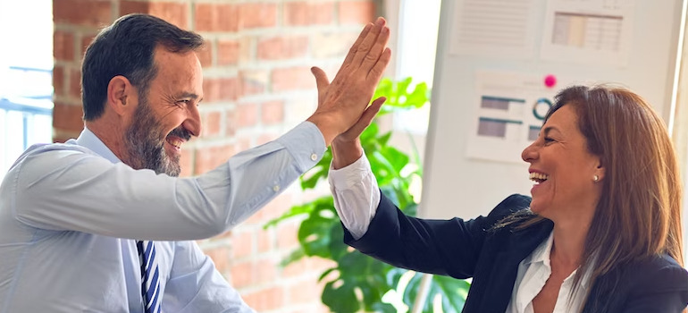 Two colleagues high fiving and discussing about the activities to boost team spirit during an office move
