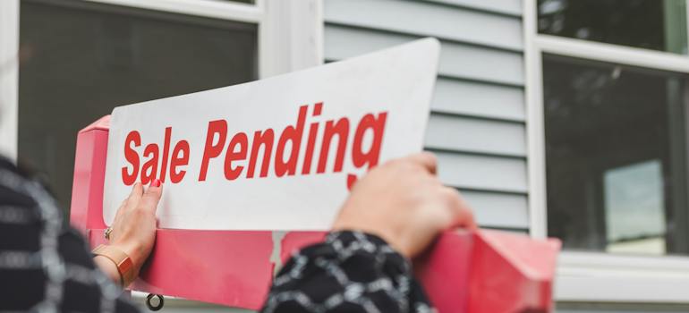 a person hanging a sale pending sign