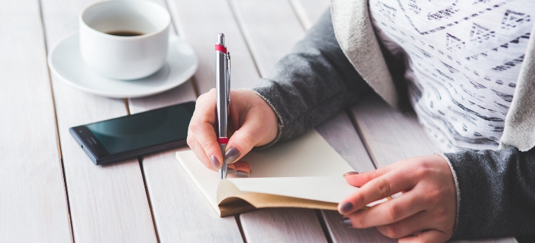 Woman writing in a notebook about what to expect and what to avoid when movers pack for you