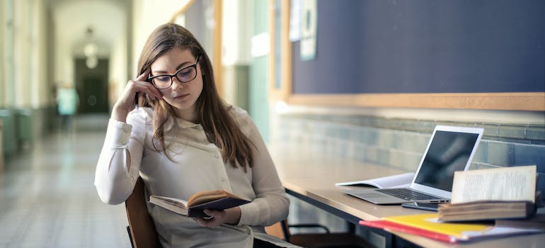 Woman in White Long Sleeve Shirt Sitting on Chair While Reading a Book