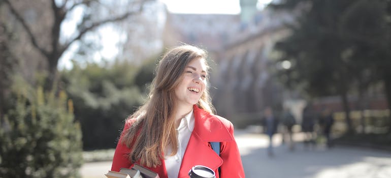 Delighted female student with takeaway coffee and books in campus