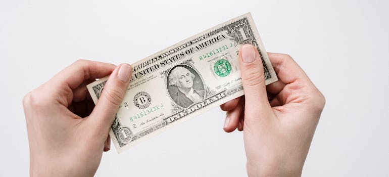 a person holding a one dollar bill and thinking whether it's cheaper to live in surrey or vancouver