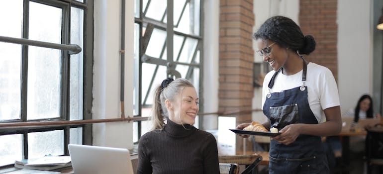 a woman sitting at the table while being served by another woman