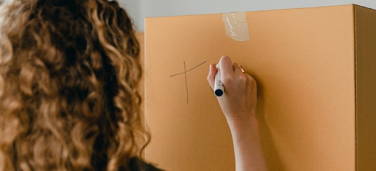A person labeling a moving box before hiring a moving & storage agency