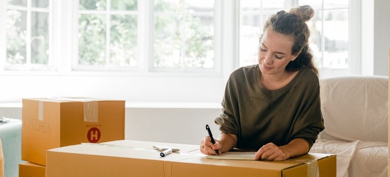 A woman writing down her moving needs on a moving box