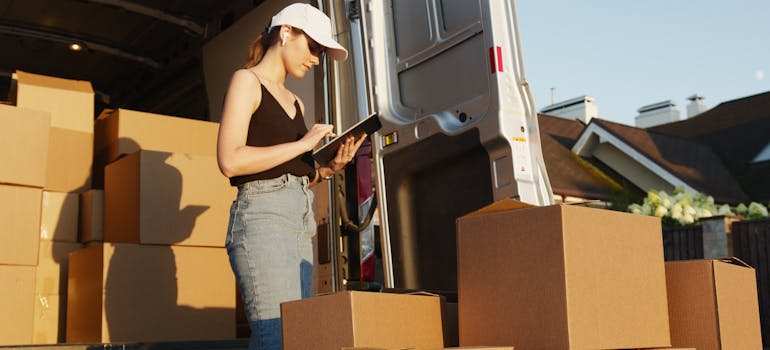 a woman with a cap reading on a tablet behind a van