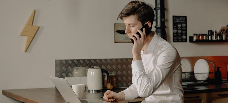 a man reading on a laptop about choosing between movers and brokers In Canada while holding a cell phone