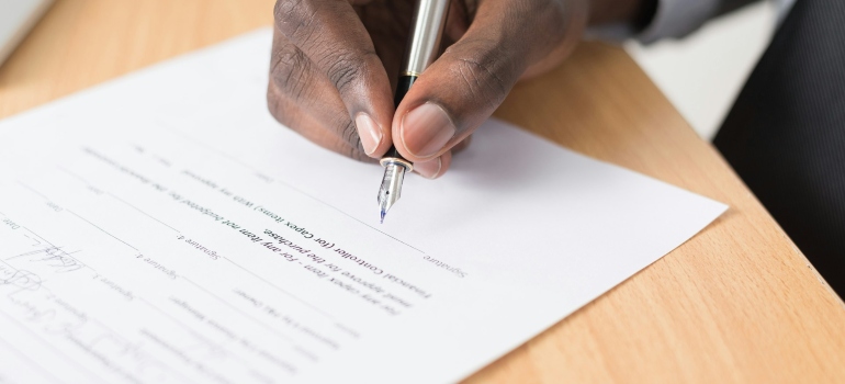 Person signing a contract while making efforts to plan a cross province relocation in Canada