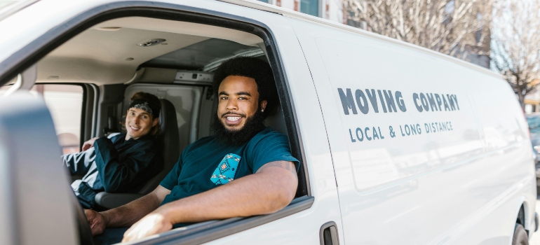 Two smiling movers in a van, ready to assist with long-distance moves, perfect for those moving to Alberta from Ontario for job seekers.