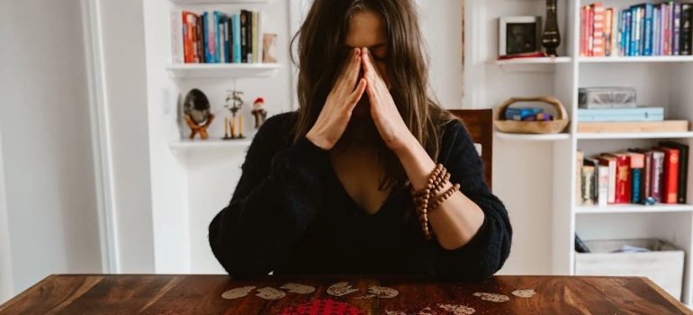 A woman sitting at the table covering her face with her hands thinking about how difficult a divorce or separation move is