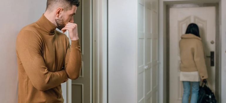 A woman at the door leaving with a bag a man standing behind and looking at her
