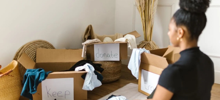 A woman looking at the group of boxes with clothes in them considering why decluttering before a move feels so emotionally liberating