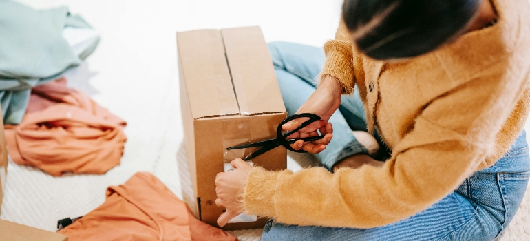 Top view of a woman using scissors to open a moving box—getting organized on move day.