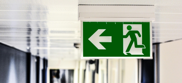Green emergency exit sign with running figure and left arrow in hallway.