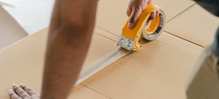 A person closing a box while trying to prepare mattresses, books, and fragile items for storage