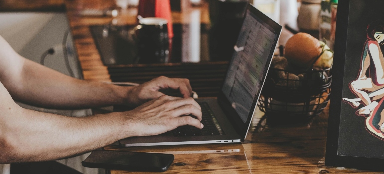 A person typing on a laptop at a kitchen counter, illustrating the mobile nature of remote work and How Remote Work Is Affecting Moving Trends in Ontario.