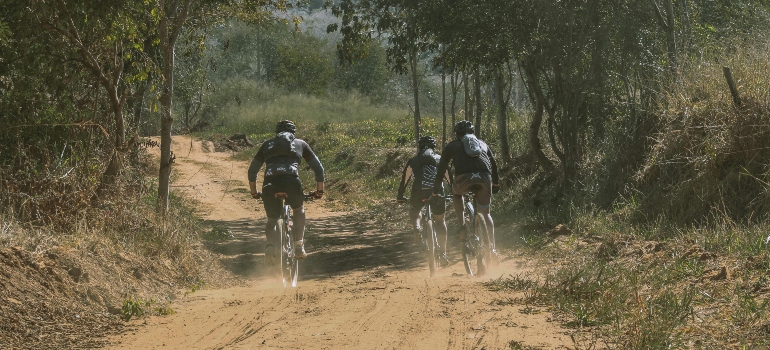 Three cyclists ride along a dusty trail surrounded by trees, enjoying the outdoors away from the rising Edmonton cost of living.
