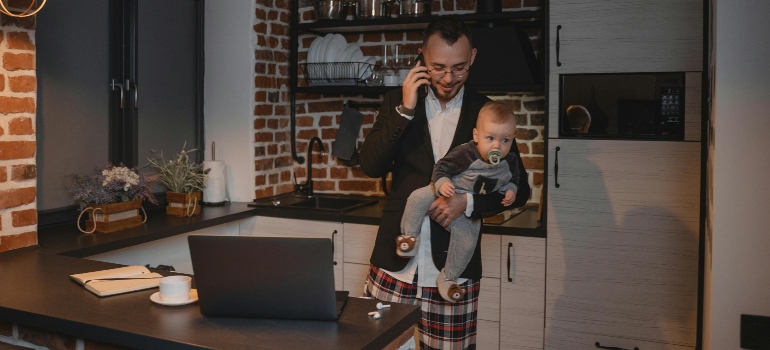 A father multitasking with a baby in hand while taking a work call in his kitchen.