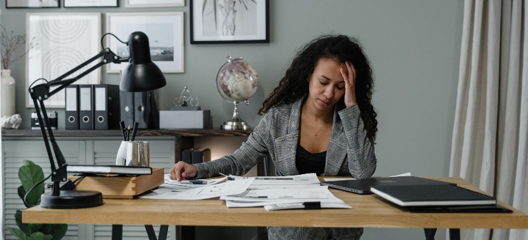 A frustrated woman surrounded by paperwork at her home desk, reflecting remote work stress.