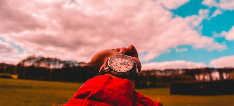 A person in a red jacket checks their watch against a dramatic sky, emphasizing timing and planning in the Dos and Don'ts of Your Long-Distance Move.