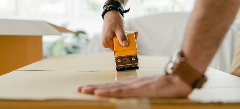 A man is using tape to pack a box.