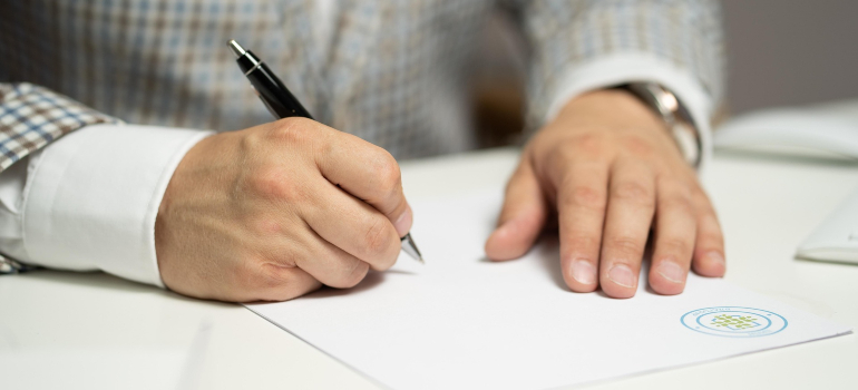 Close-up of a hand signing a printed document with a pen on a desk.