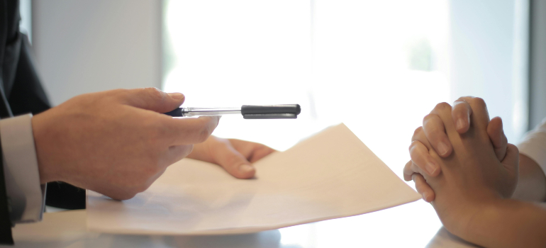 Advisor handing a pen and paperwork to a client with folded hands during a meeting.