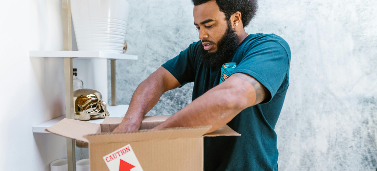Mover packing a caution-labeled box indoors; careful packing shows traits of reliable cross border moving companies.