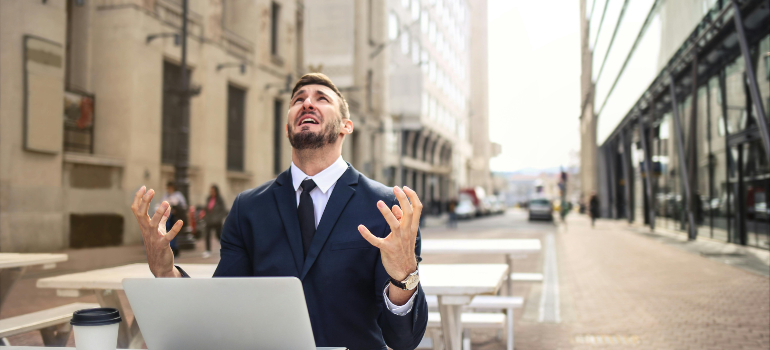 Frustrated man at a laptop outdoors after a bad mover choice, underscoring red flags and traits of reliable cross border moving companies.