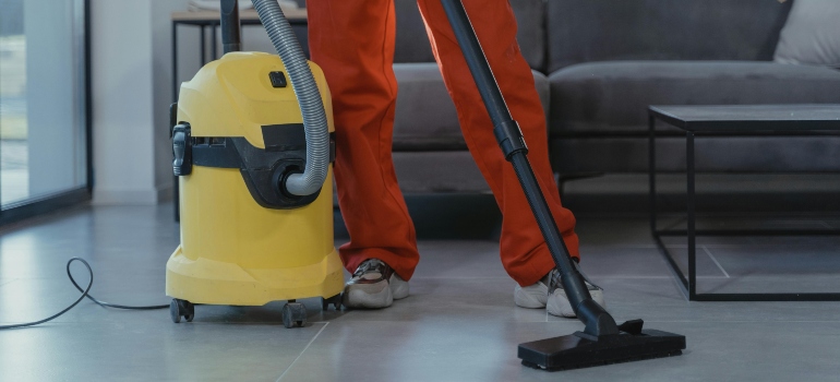 A person is cleaning the floors with a vacuum cleaner and thinking about safeguarding hardwood floors during relocations.