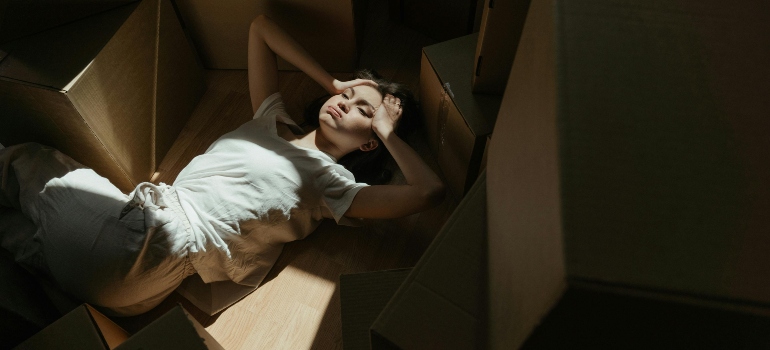 Stressed woman lying on the floor surrounded by moving boxes, wondering what can you do when your movers are late and the schedule falls behind.