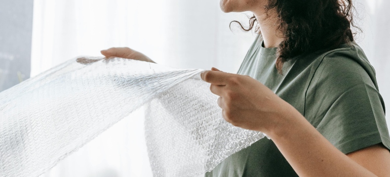 A woman is using bubble wrap to pack her stuff for relocation.