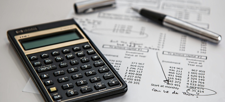 Calculator on top of financial documents with two pens, showing budgeting and cost planning.