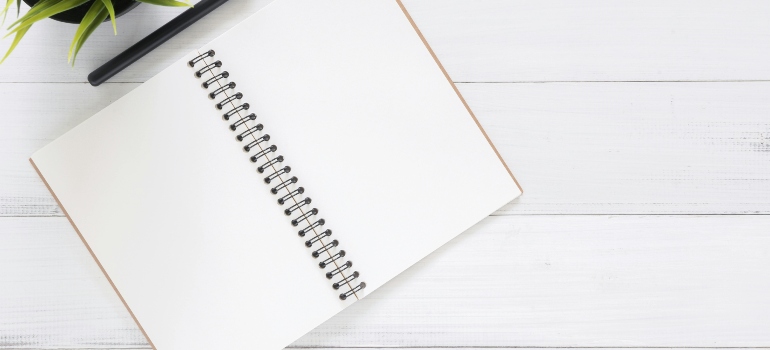 Open blank spiral notebook on a white desk with a plant in the corner, ready for notes and planning.