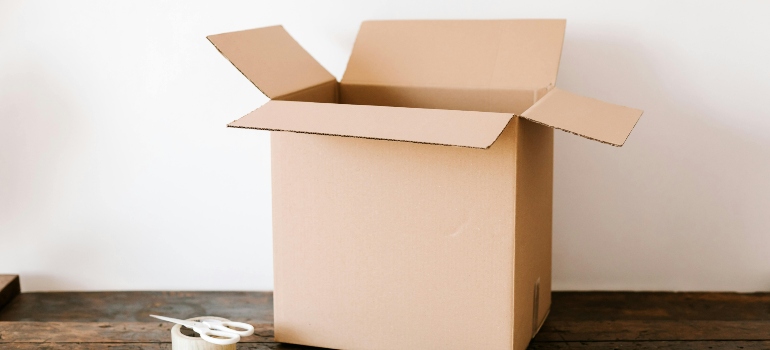 Open cardboard box on a table with packing tape and scissors nearby.