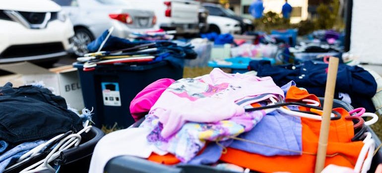 Outdoor garage sale with clothing racks and cars nearby as homeowners organize a yard sale before moving and sell unwanted items.
