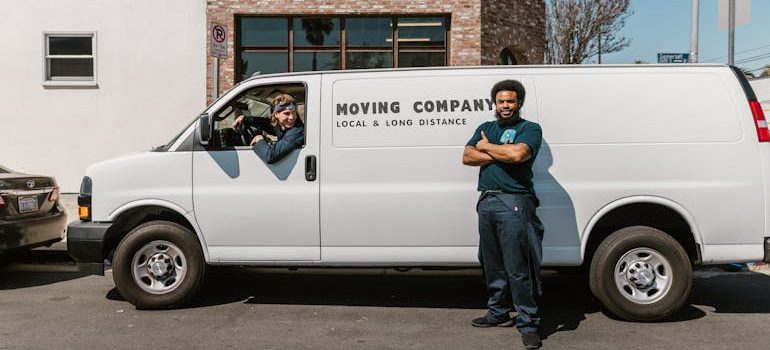 Two professional movers standing in front of a moving company van with the company logo, ready to assist with a residential relocation.