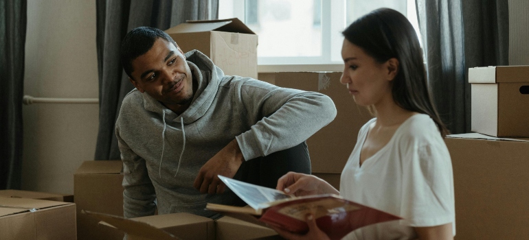 A man in a gray sweater looks at a woman in a white shirt sitting beside moving boxes during a move from Scarborough to Thornhill