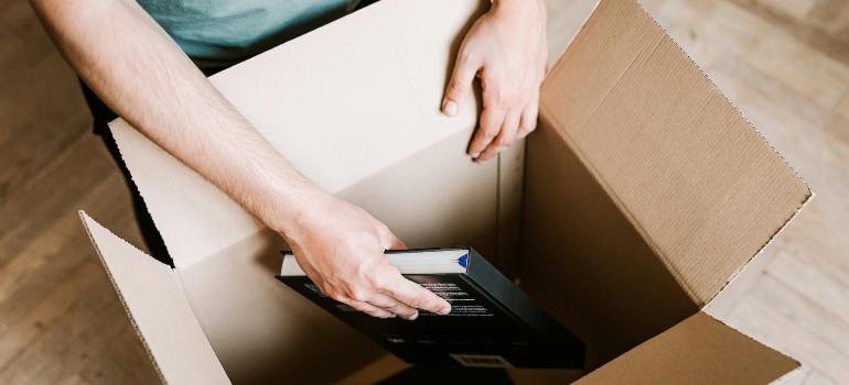 Crop man packing books in carton box while choosing the right office movers in Toronto