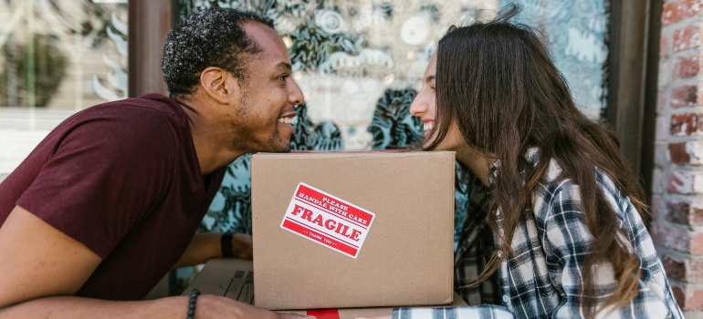 A man and a woman smile at each other while leaning on moving boxes