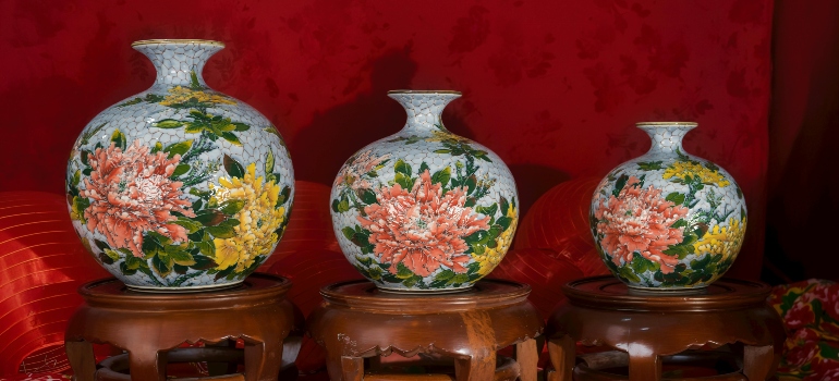 Three antique ceramic vases with floral designs displayed on wooden stands against red background.