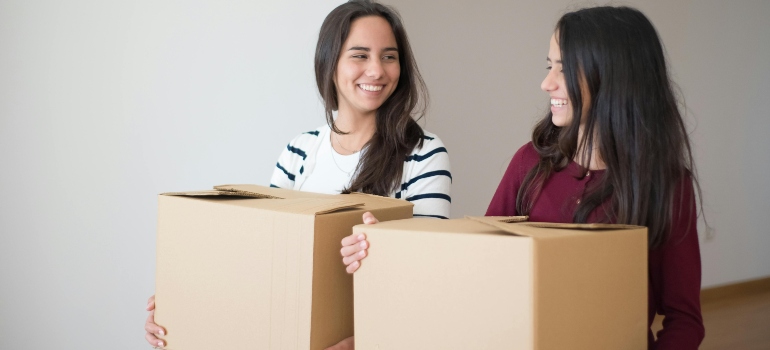 Two friends carrying boxes and smiling during a move.