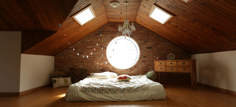 Attic bedroom with wooden ceiling, chandelier, and furniture requiring careful moving preparation.