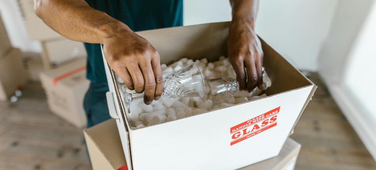 Worker placing delicate glassware into padded box with protective packing materials instead of low-priced relocation supplies.