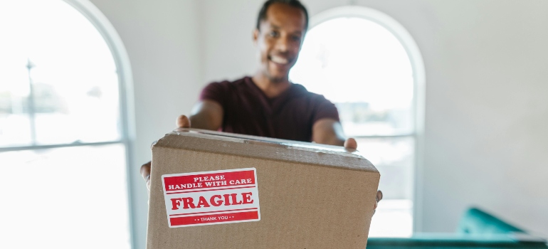 Man holding a cardboard box labeled fragile to protect commonly damaged articles during relocation.