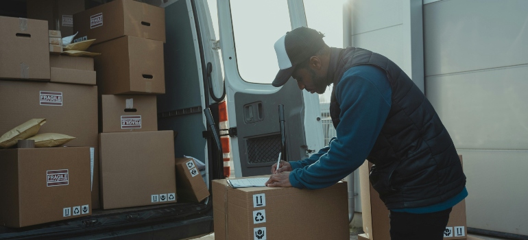 Mover writing on labeled boxes inside moving truck to ensure proper tracking and secure transport.