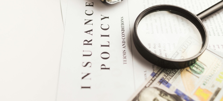Close-up of insurance policy document with magnifying glass and cash, illustrating coverage details and misconceptions about moving.