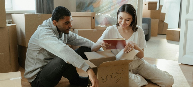 Newly married couple opening a box of books while settling into their apartment.