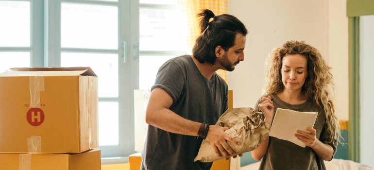 Couple packing household items and planning how to relocate as a newly married couple while organizing boxes in their new home.